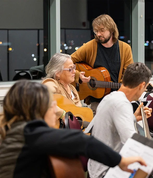 Participants play acoustic guitars during a community music education workshop.