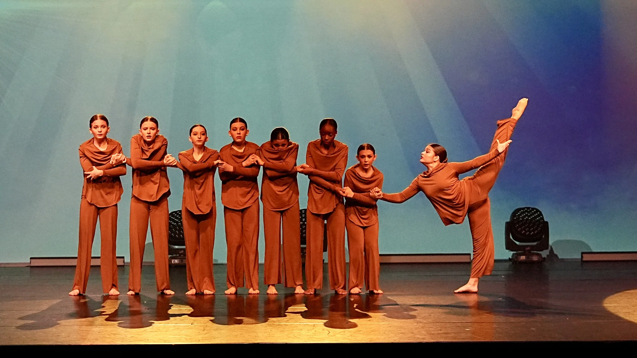 Dancers in orange on stage in a line.