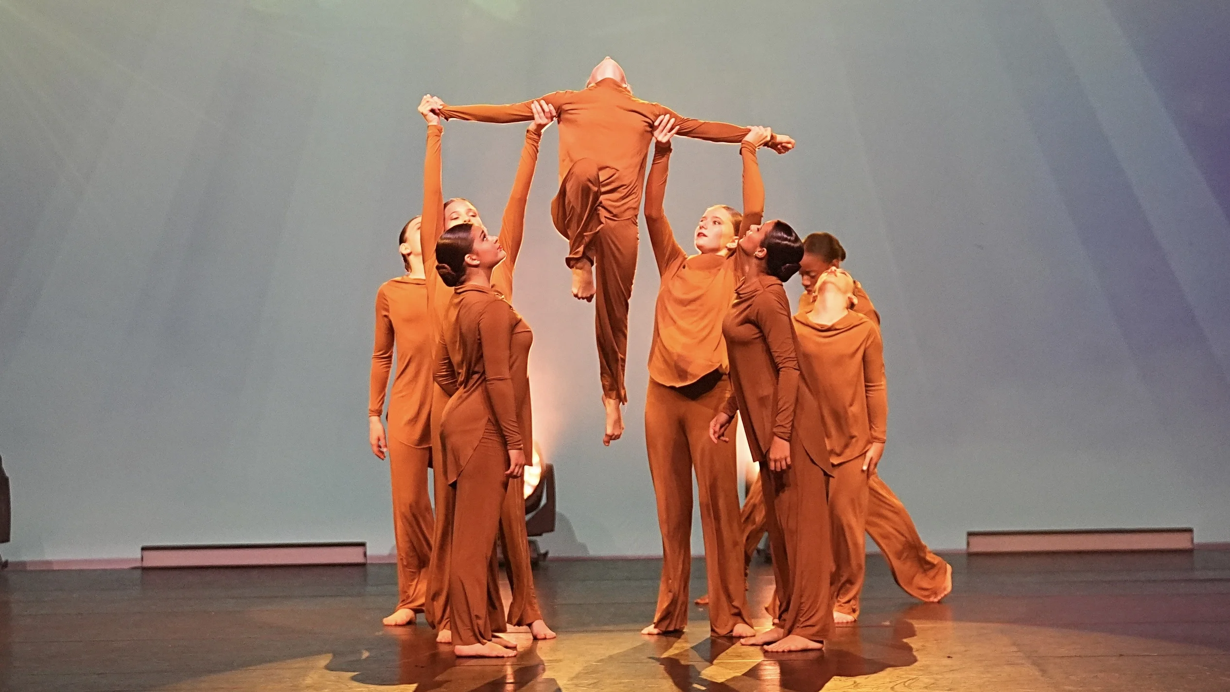 ncers in orange on stage holding up a single dancer.
