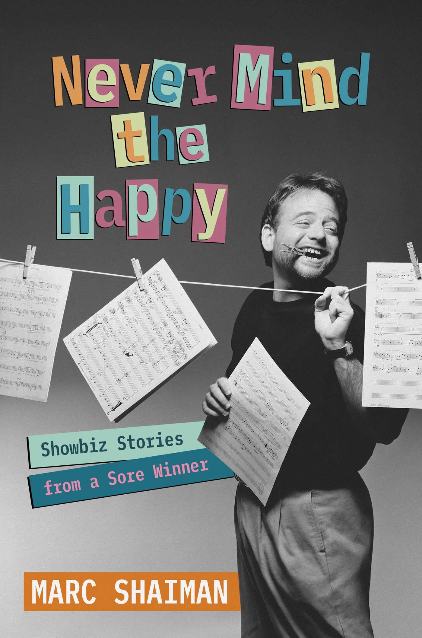 Black‑and‑white book cover showing a person standing and holding multiple sheets of handwritten music. Additional music sheets hang from a clothesline stretched across the image. The title Never Mind the Happy appears in colorful, cut‑out style letters at the top. A teal and blue label near the bottom reads Showbiz Stories from a Sore Winner. The author’s name, Marc Shaiman, appears in white text on an orange block at the bottom.