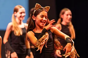 Student smiling as they perform as a cat. More student cats in background.