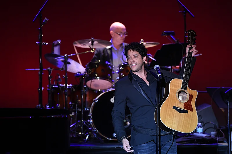 Lead singer performing on stage in front of drum kit during energetic rock concert show holding guitar.