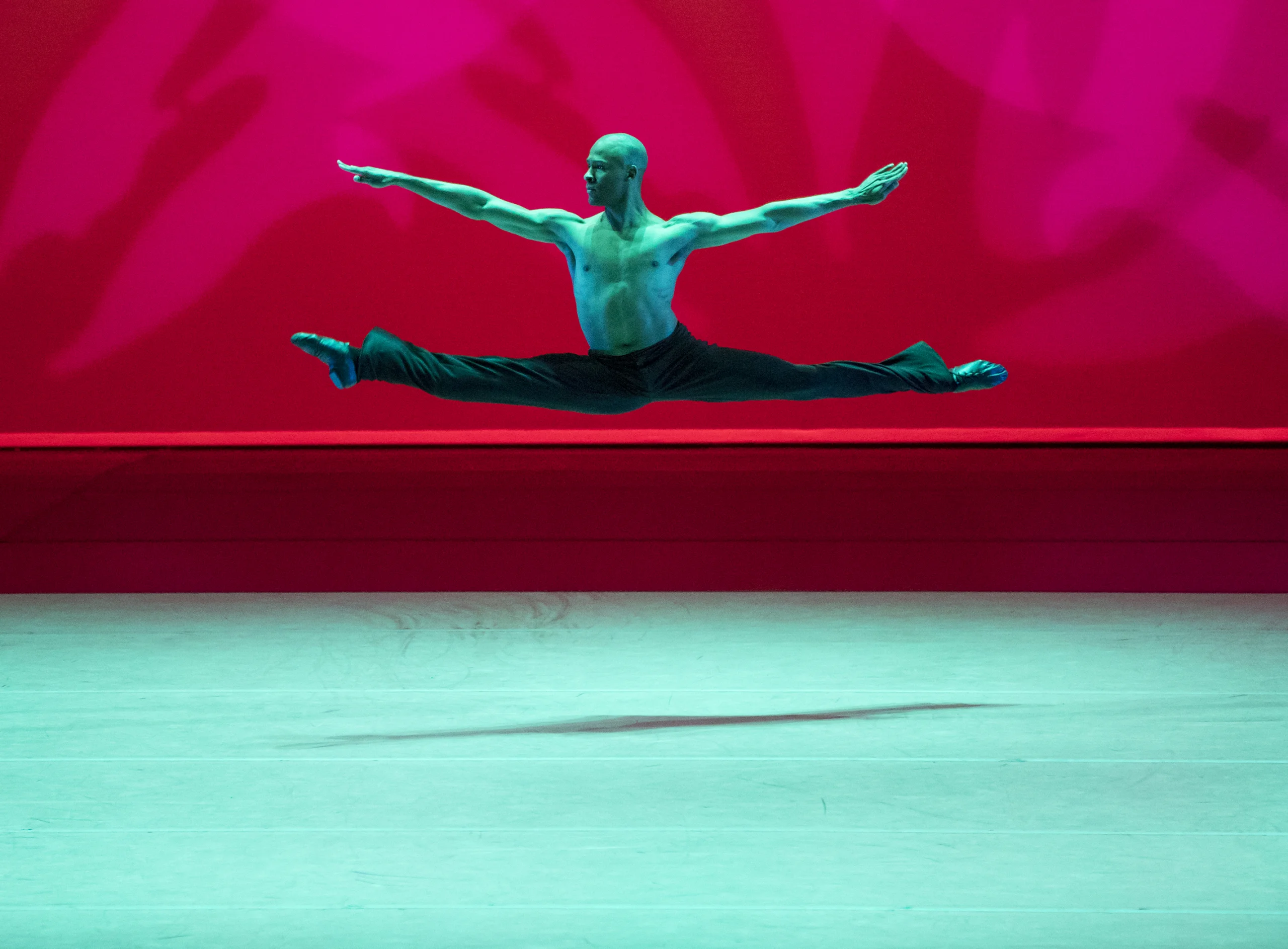 ©Paul Kolnik Ballet dancer midair in a split leap on stage against a vivid red background.