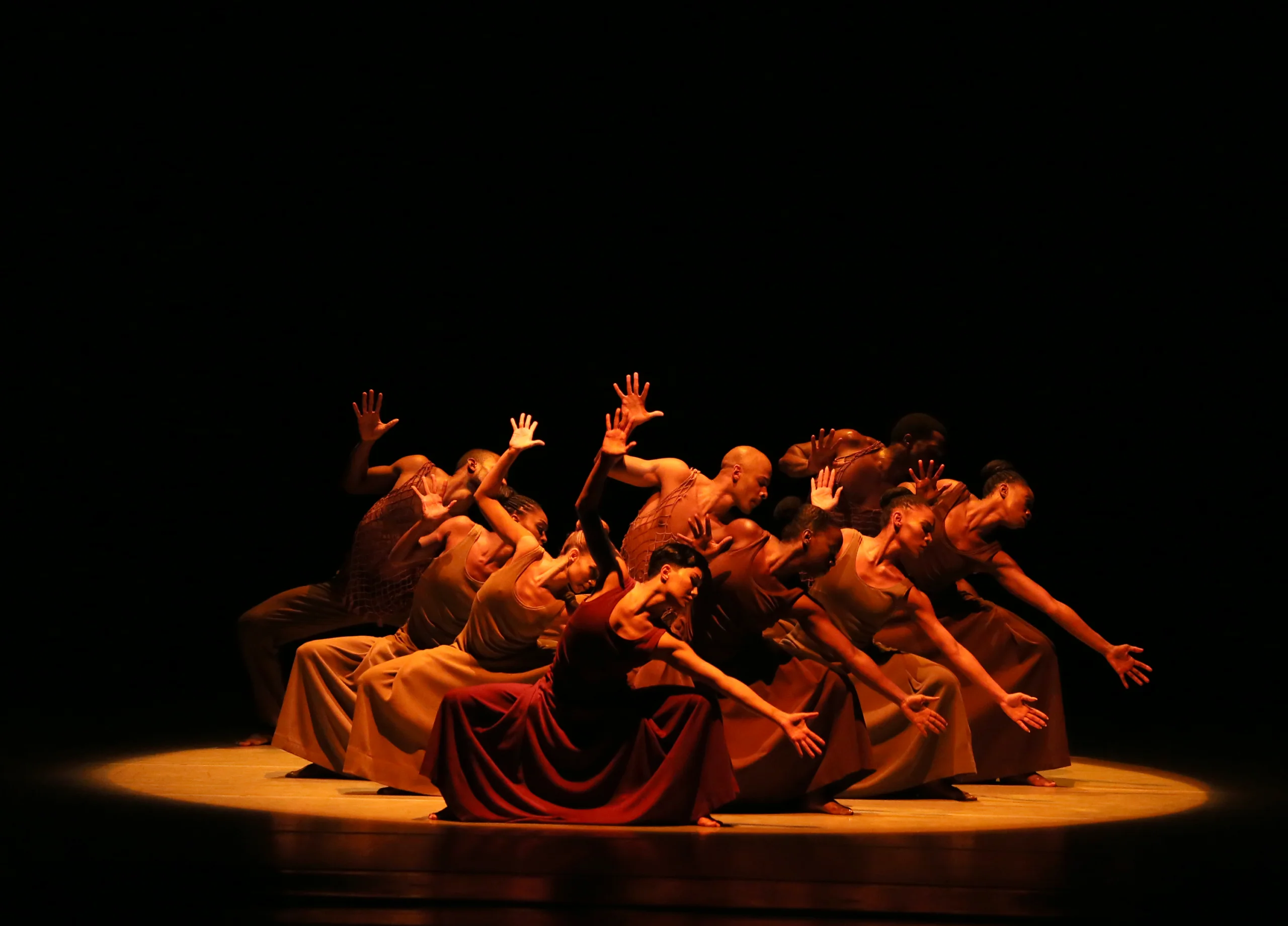 Inside the 2022 Ailey Spring Gala performance at the David Koch Theater at Lincoln Center in New York City, New York on Thursday, June 16, 2022. Group of dancers leaning forward in unison with raised hands under warm stage lighting.