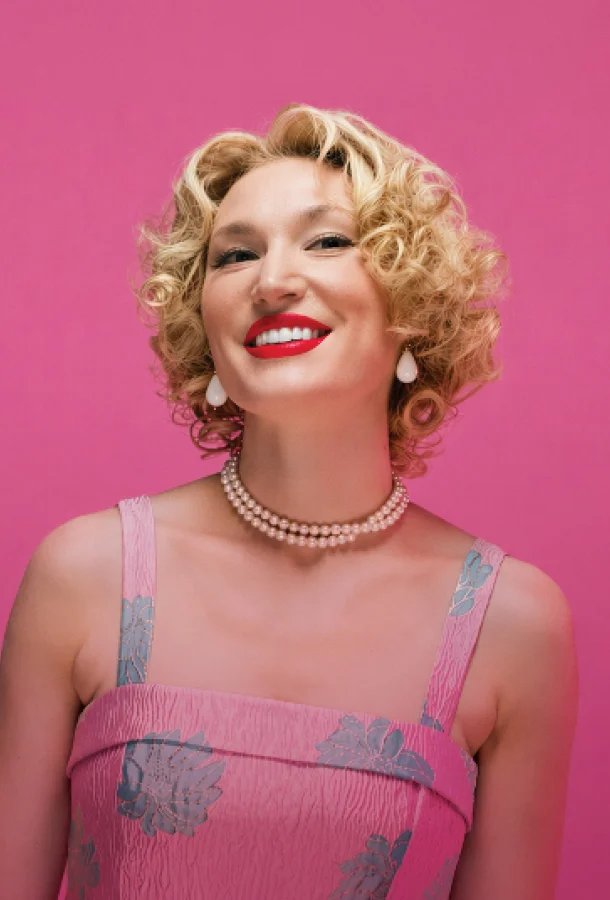 Performer in a pink vintage-style dress with pearl necklace against a pink background, representing a Doris Day tribute.