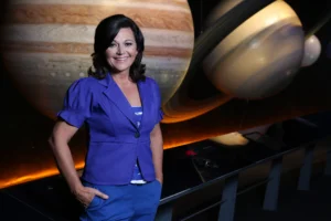 A woman stands in front of a space exhibit featuring large models of Jupiter and Saturn.