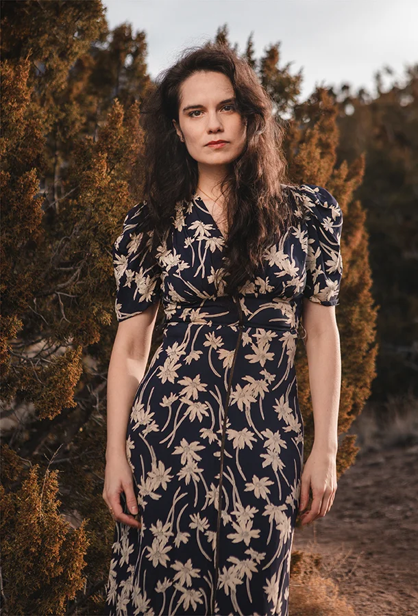 Julia Keefe wearing a floral dress standing in a desert-like landscape.