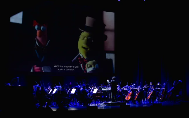 Disney’s The Muppet Christmas Carol Live in Concert featuring a live orchestra performing the film score beneath a large screen showing scenes from the holiday classic.
