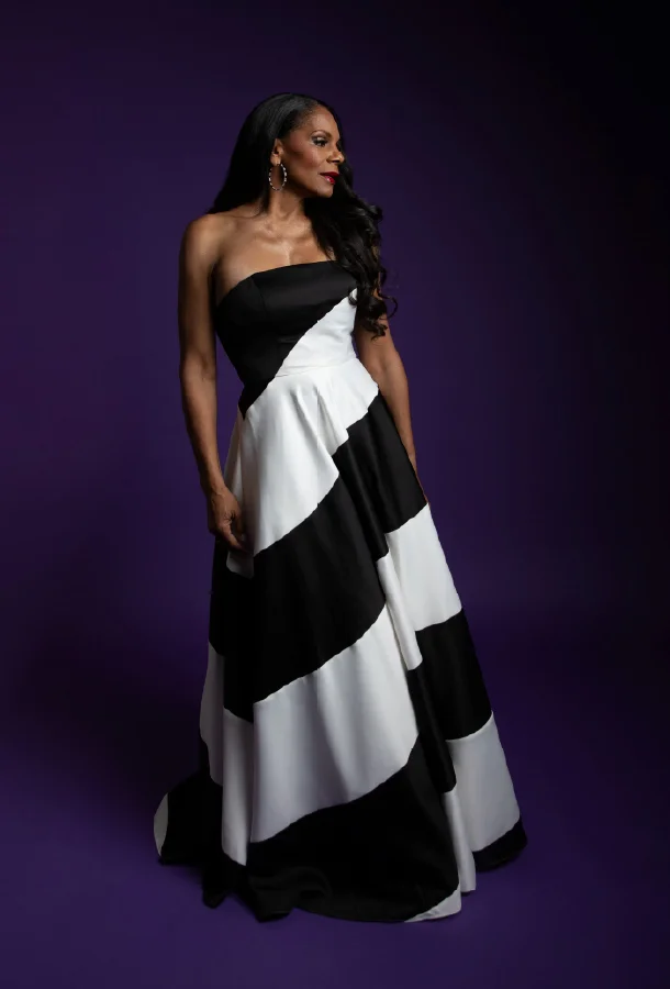 Performer in a black-and-white formal gown posed against a purple background.