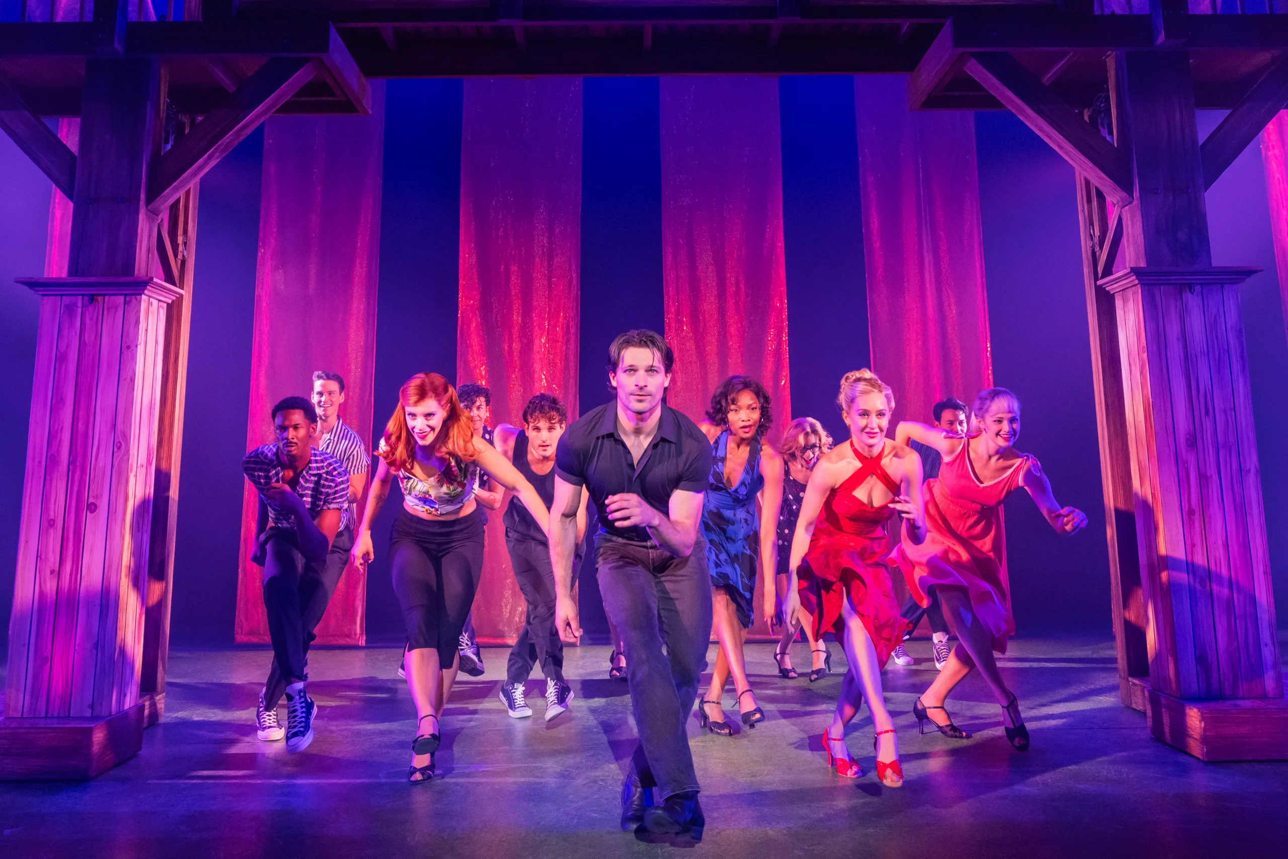 Dirty Dancing: The Musical featuring a memorable dance scene with lead performers beneath dramatic pink stage lighting.