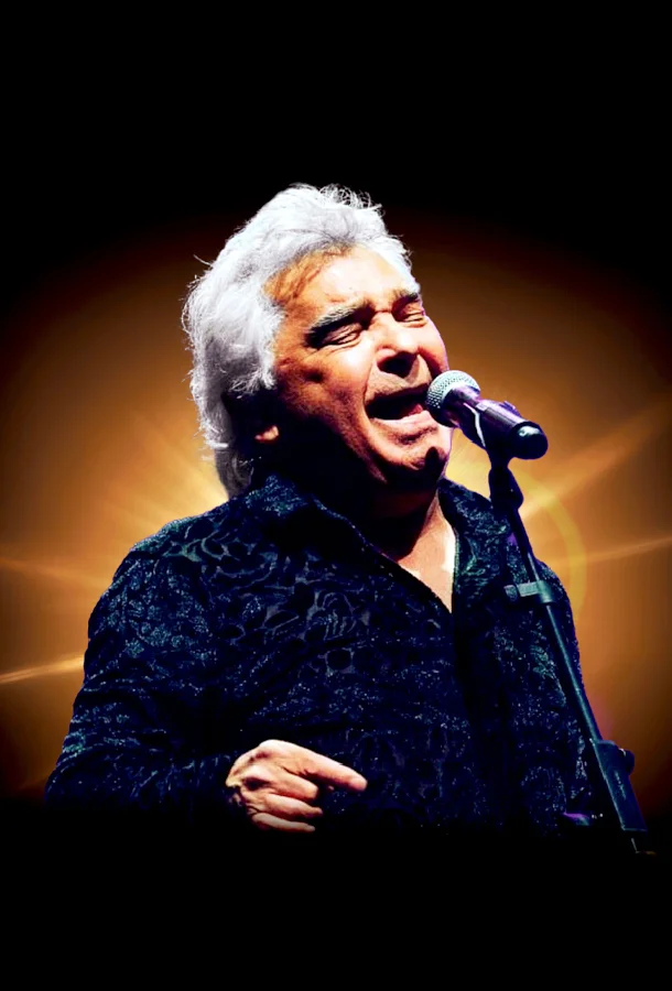Performer in a black tuxedo holding a microphone with a city skyline in the background.