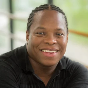 Professional headshot of Larry Albright wearing a black collared shirt, seated indoors with a softly blurred background.