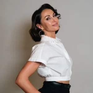 Alt Text: Professional portrait of Natalia Maidiuk wearing a white blouse with a lace collar and hoop earrings, posed against a light gray background.