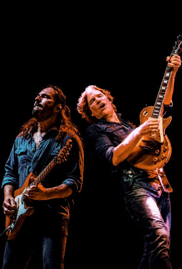 Two guitarists performing together onstage during a live rock concert.