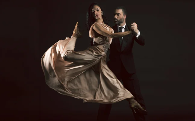 Two dancers performing a dramatic tango pose, with a flowing gown and formal attire against a dark background.