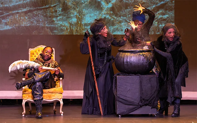 A scene on stage with the bard siting in chair with caldrone.