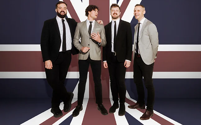 Four individuals standing in front of a large British flag.