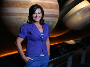 A woman stands in front of a space exhibit featuring large models of Jupiter and Saturn.