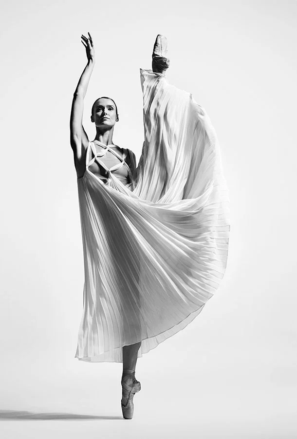 Ballet dancer performing en pointe with a high leg extension in a flowing pleated costume.