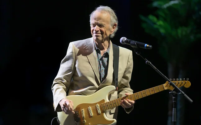 Al Jardine playing an electric guitar during a live concert performance.