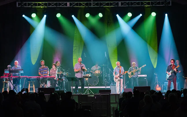 Band performing live on stage under green and blue concert lighting.