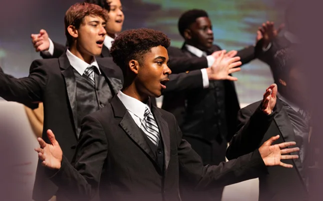 Youth performers sing on stage in coordinated formal costumes during a Broadway showcase performance.