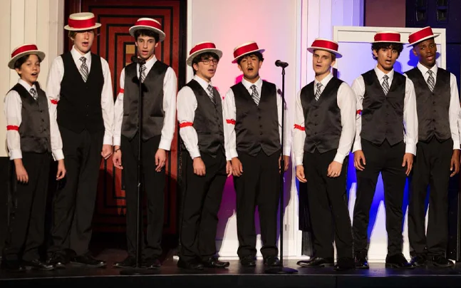 Student performers sing together under blue stage lighting during a theatrical music performance.