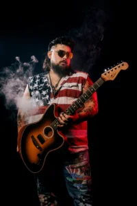 Bryant Thomas holding an acoustic-electric guitar against a dark background with dramatic red and blue stage lighting and drifting smoke effects.
