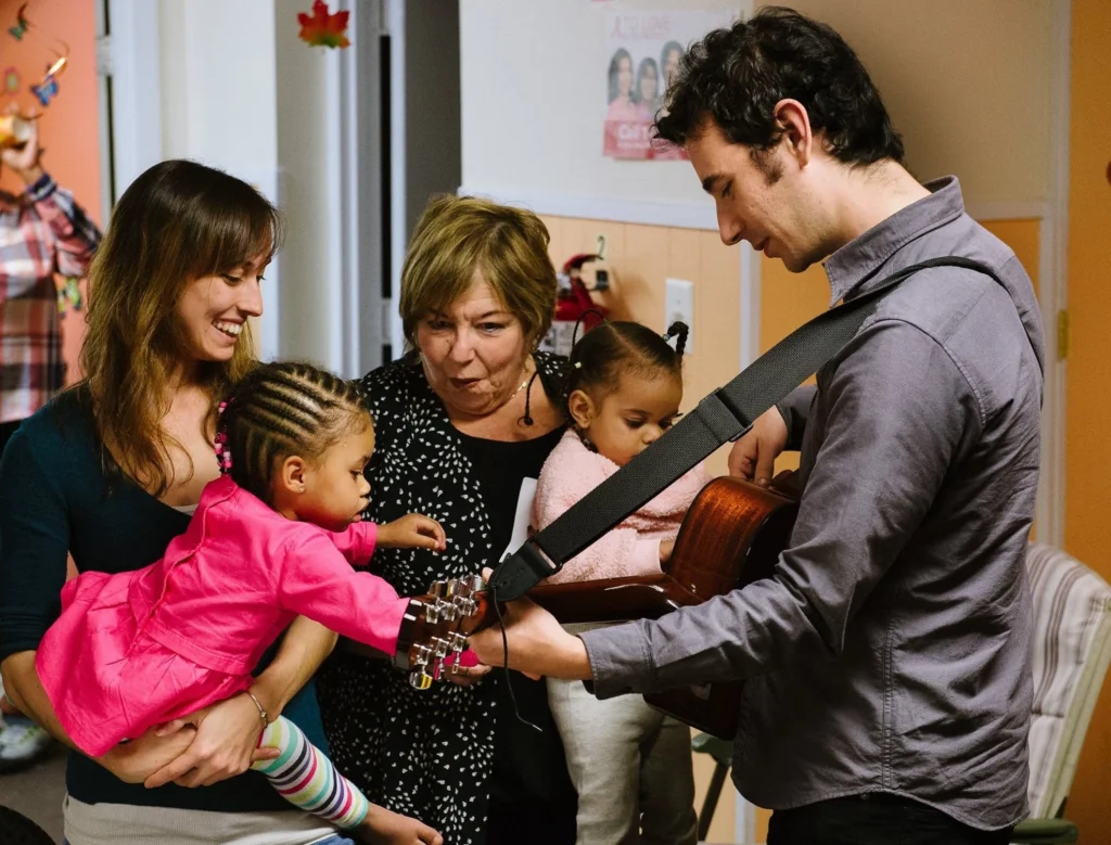 Guitarist shows two women and two babies his instrument.