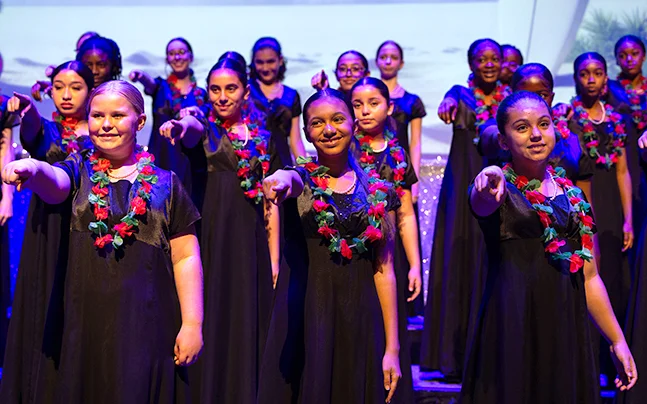Student choir on riser pointing at audience.