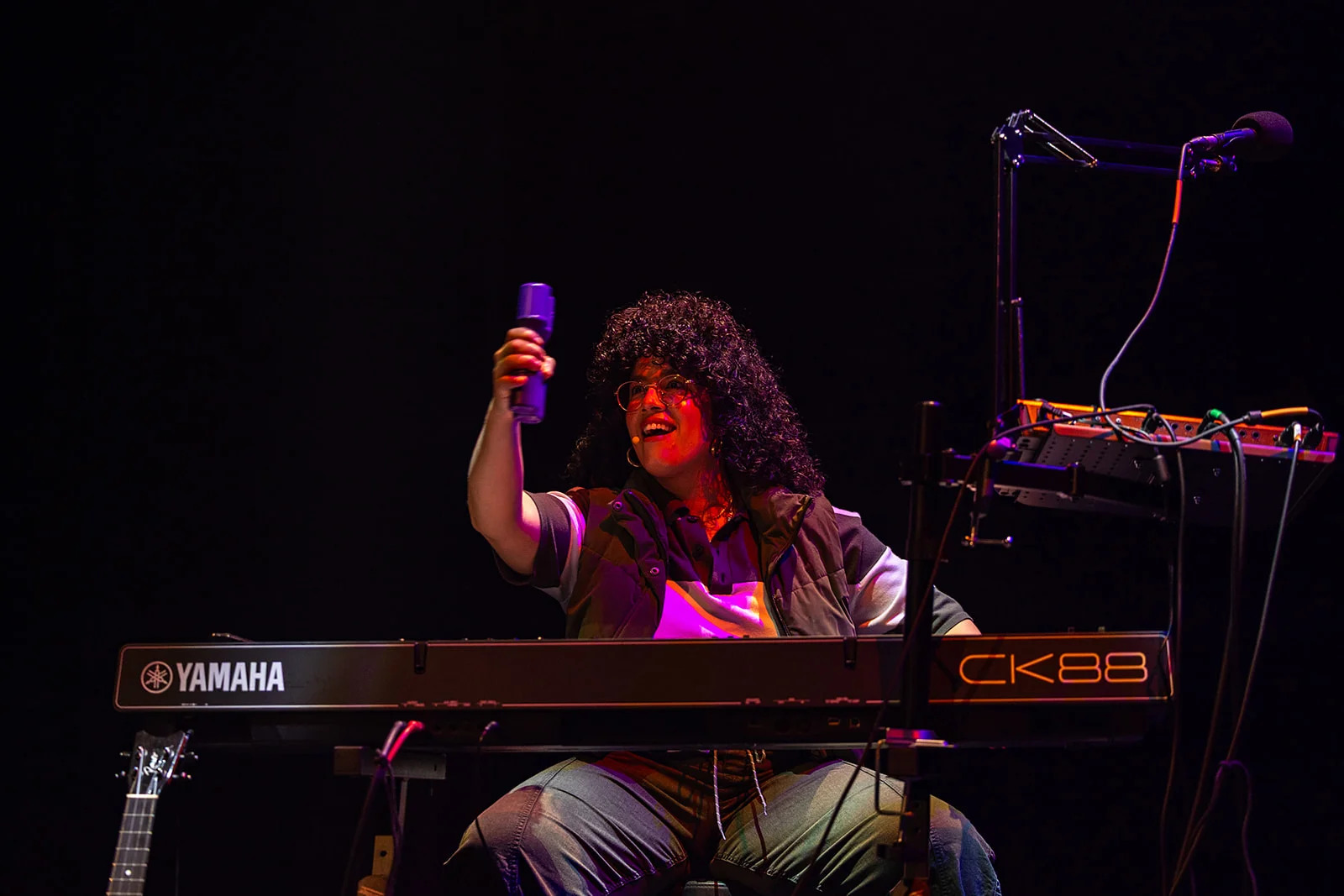Actress singing at keyboard with sound shakers in mood lighting.